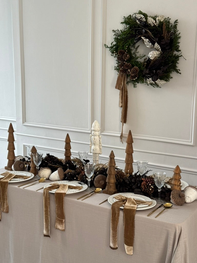 Camino de mesa Mocha con eucalipto preservado y ornamentos dorados navideños.
