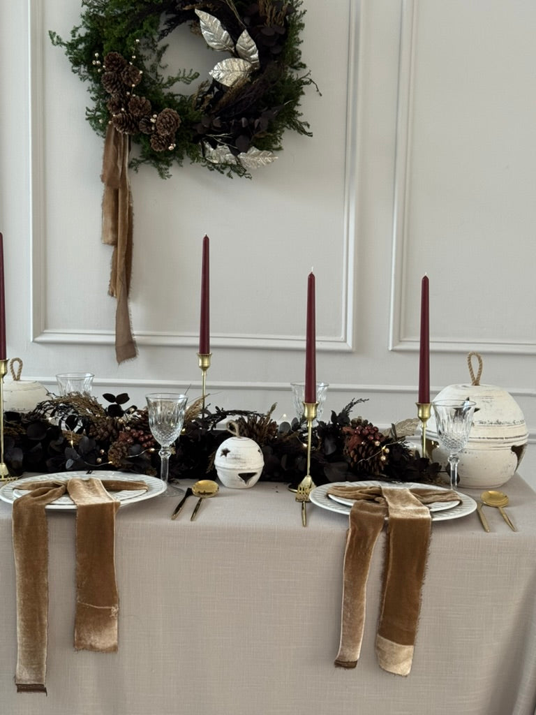 Camino de mesa largo con tonos mocha, piñas naturales y ornamentos bronce.
