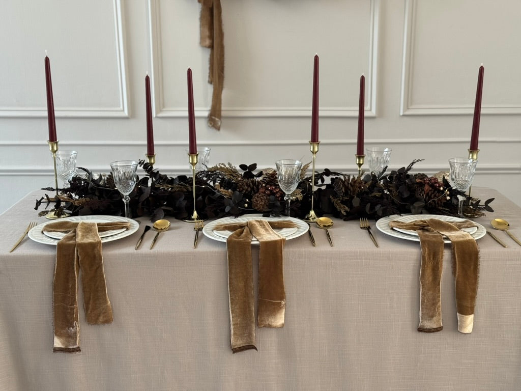 Camino de mesa navideño en tonos mocha con piñas naturales y ornamentos bronce.
