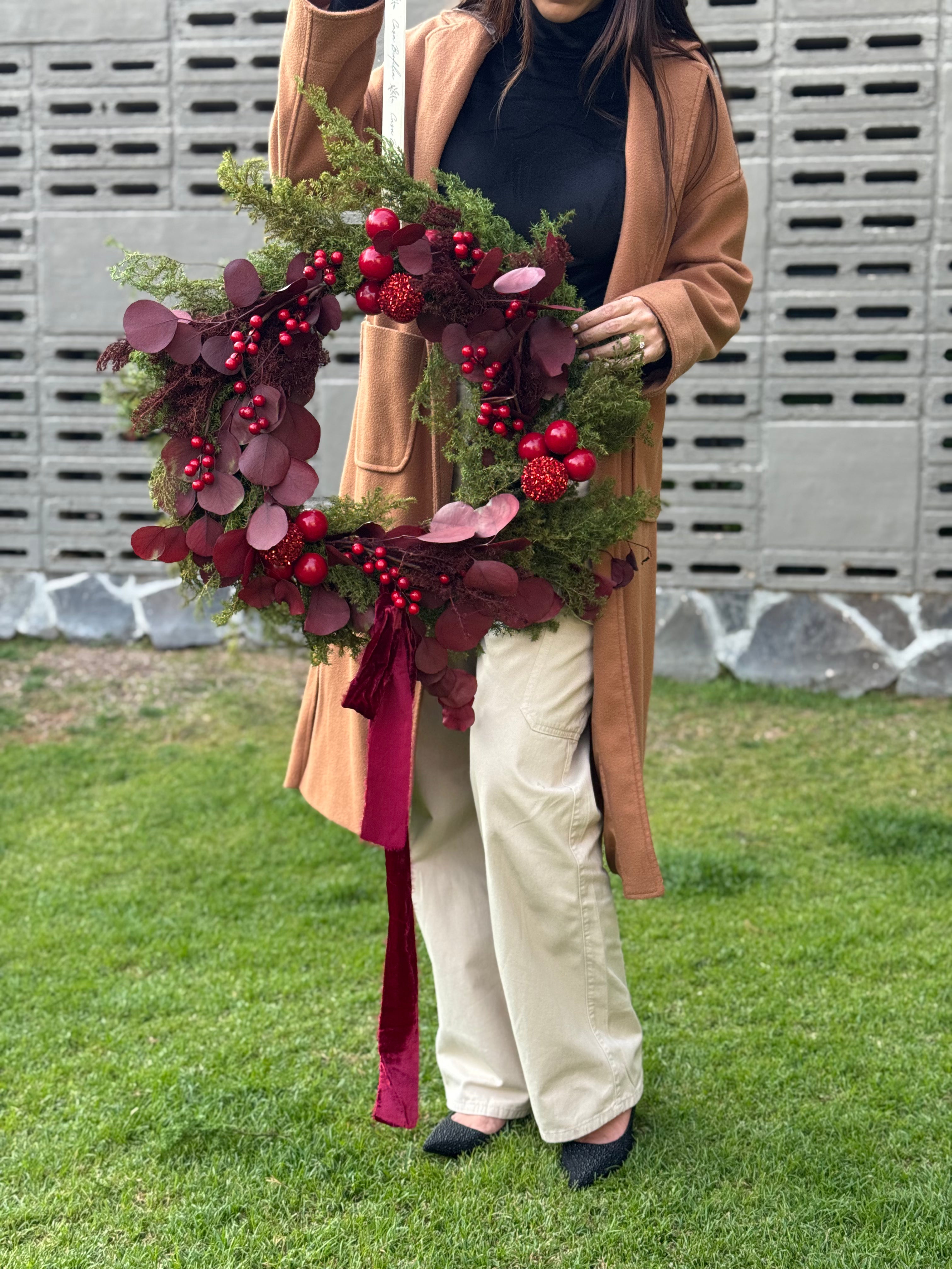 Corona navideña de 60 cm con pino verde, eucalipto silver en tono tinto, esferas rojas brillantes, cerezas artificiales y moño de terciopelo tinto.